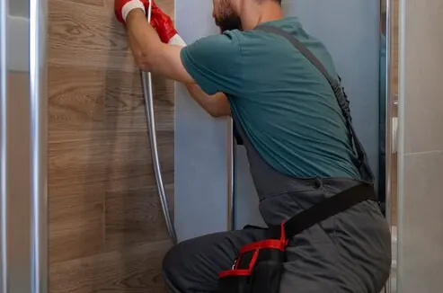 Plumber kneeling in the shower cubicle, next to the drain pipe